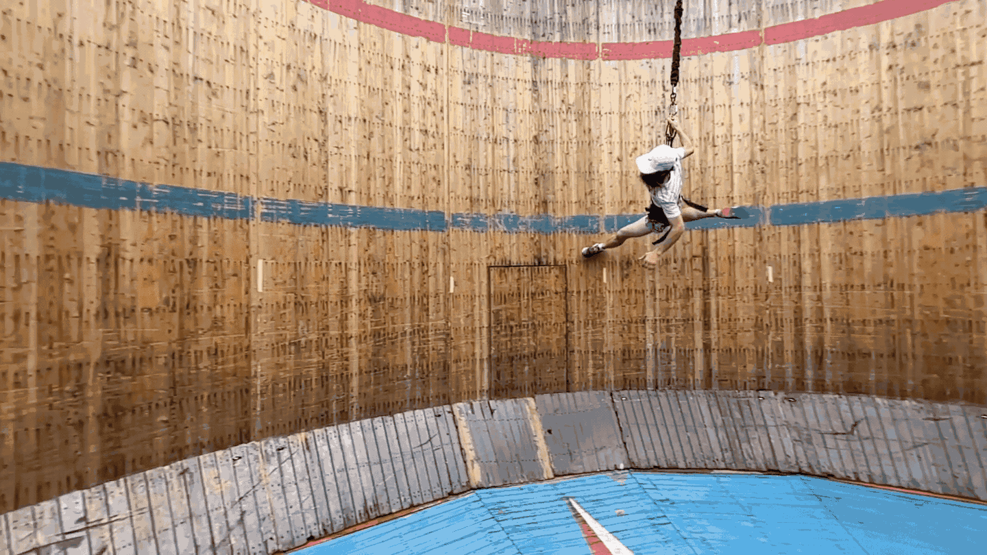 In this gif, a man in a white shirt and hat is running along the interior wall of a wooden cylinder in an attempt to emulate low-gravity exercise on the moon.