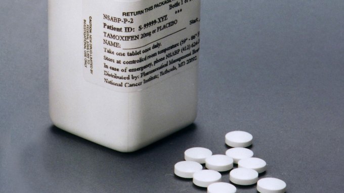 Some round white pills sit beside a pill bottle labeled tamoxifen, which is a popular breast cancer drug.